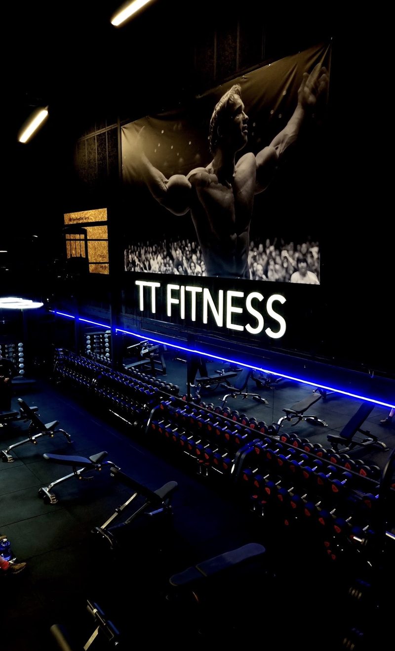 The free-weight area beneath the TT Fitness mural, with rows of dumbbells and blue lighting